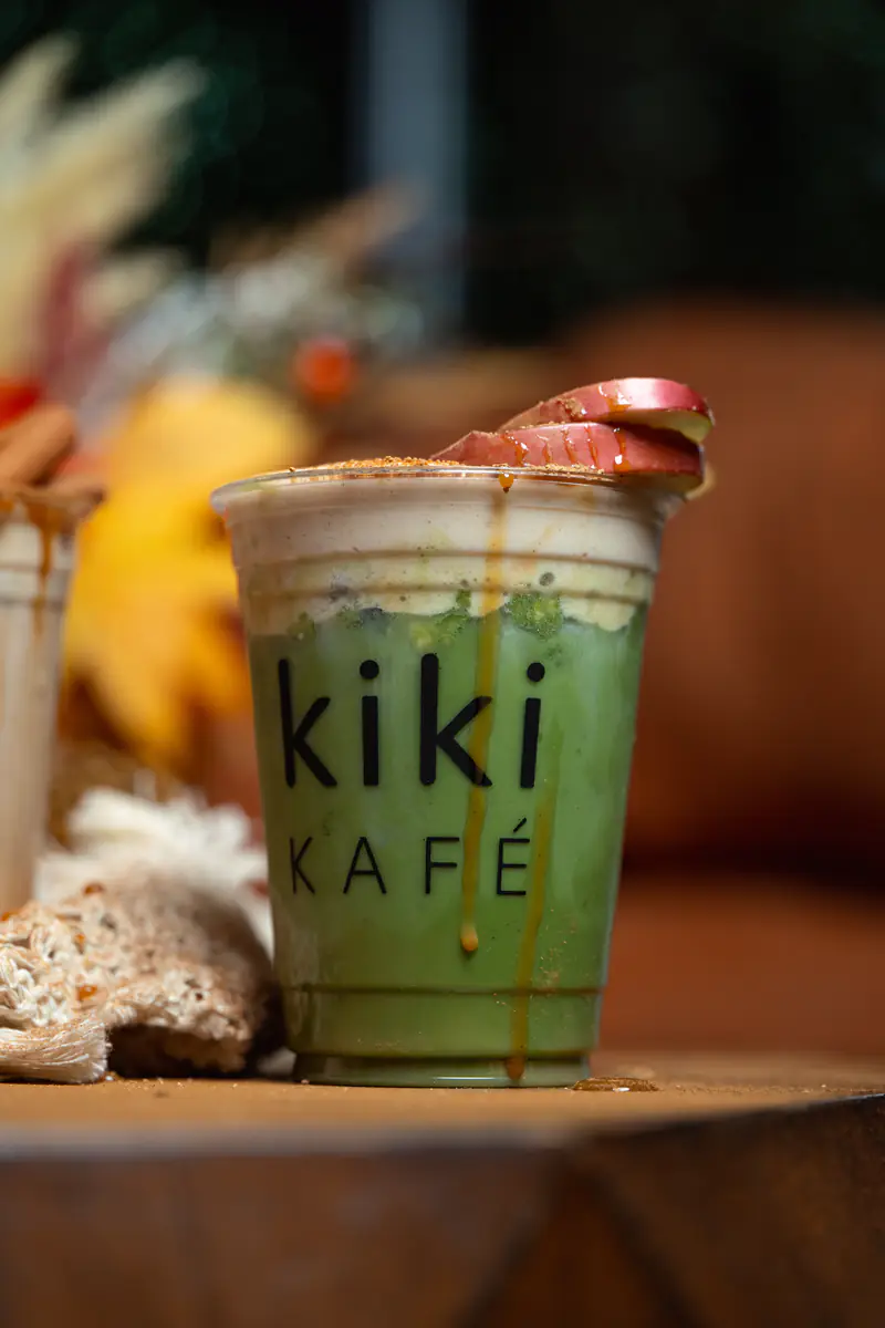 Caramelized apple matcha with yellow fall leaves behind it at Kiki Kafé