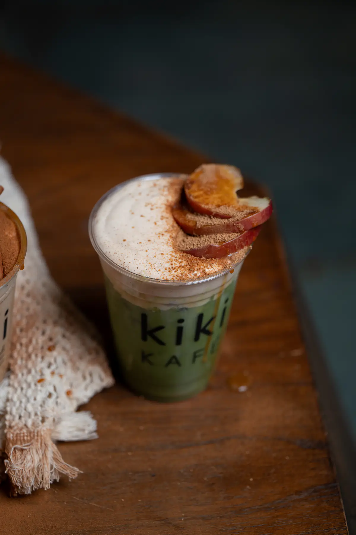 Caramelized apple matcha with apple slices on a dark wood counter at Kiki Kafé