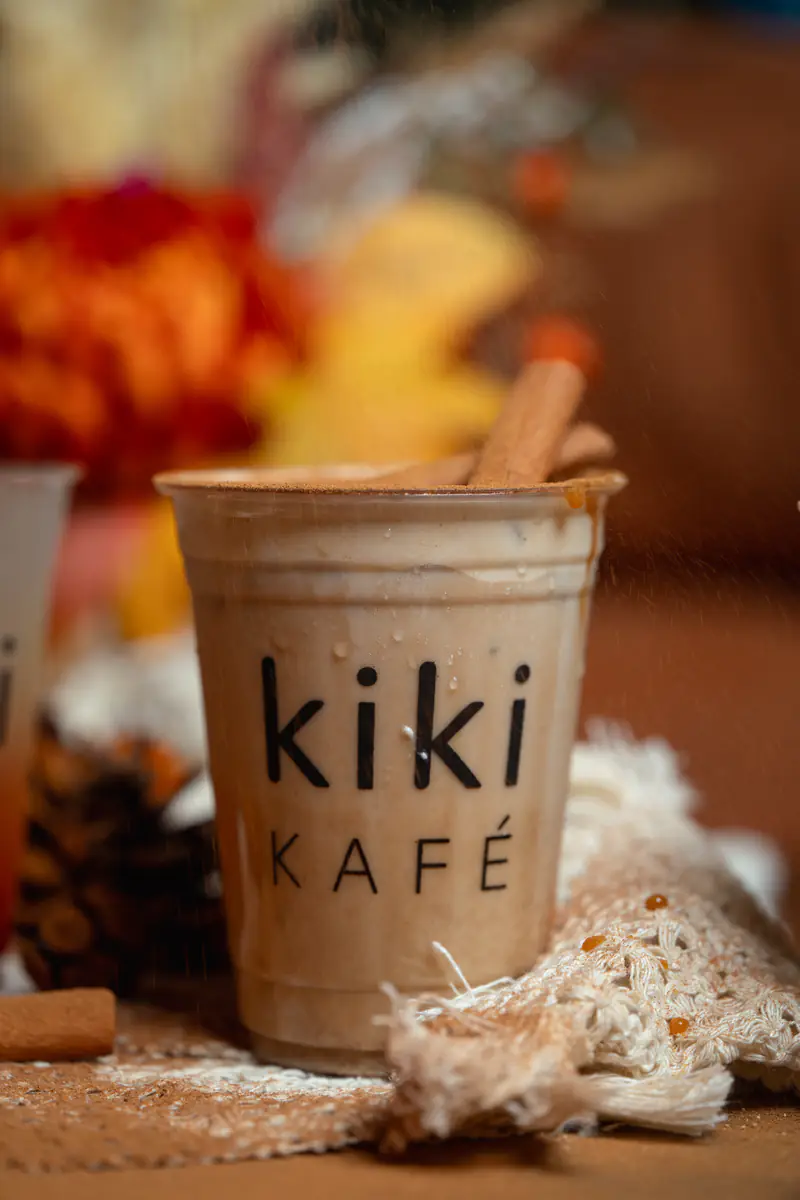 Cinnamon-dusted latte in a Kiki Kafé cup with cinnamon sticks and red-orange fall flowers