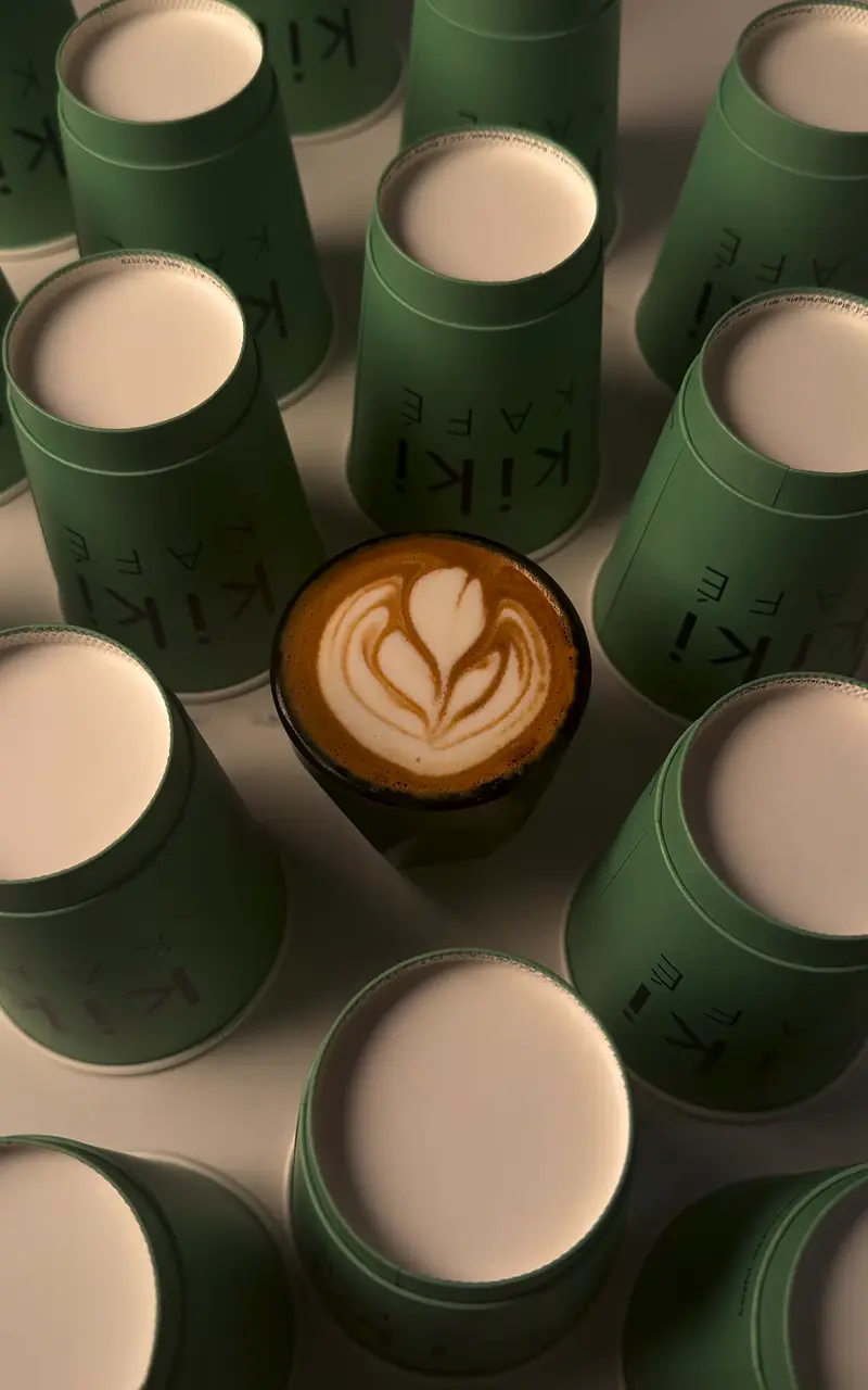 Cortado with latte art surrounded by green meet me at kiki cups