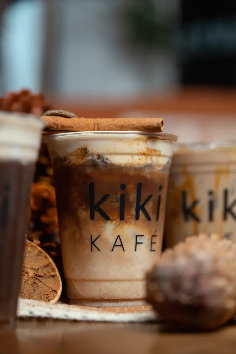 Iced fall drink in a Kiki Kafé cup with a cinnamon stick, dried orange and pinecones