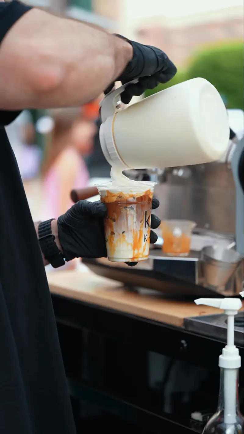Barista pouring milk into an iced caramel latte at the Kiki Kart