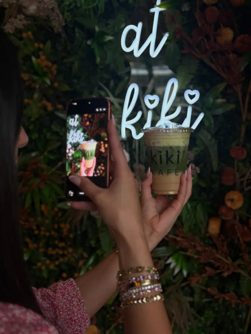 Iced matcha latte held up in front of the at kiki neon sign