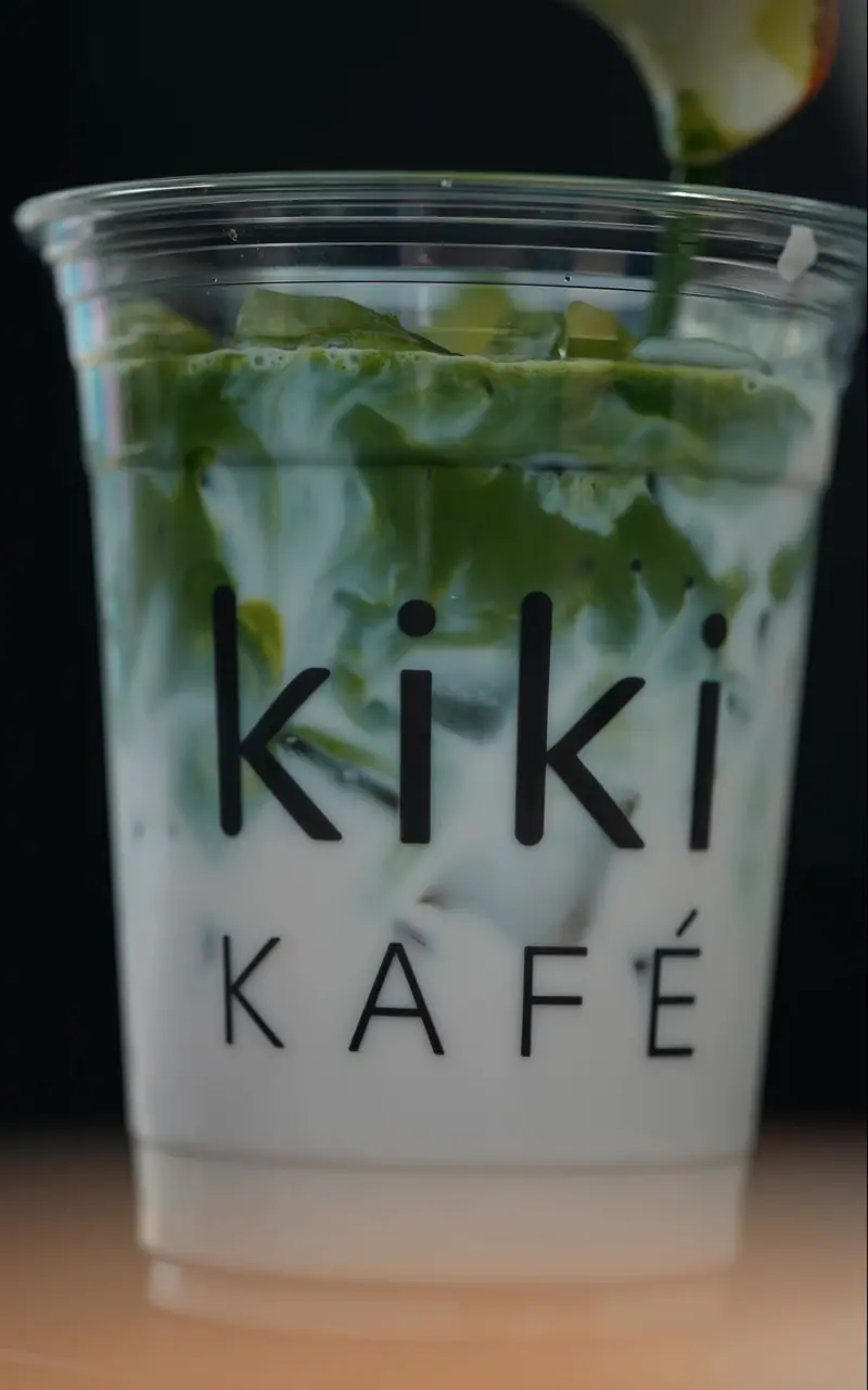 Matcha pouring over ice and milk in a clear Kiki Kafé cup