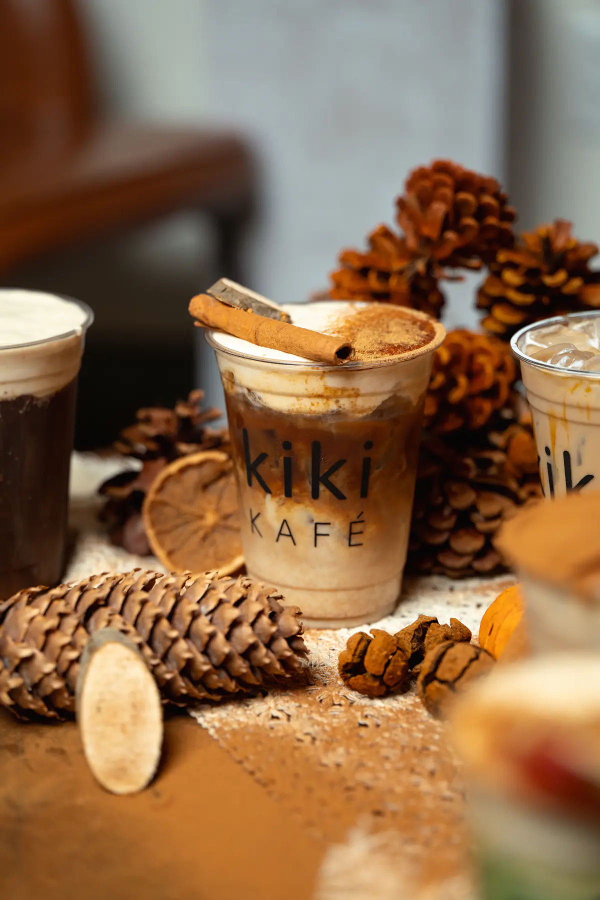 Three Kiki Kafé fall drinks styled with pinecones, cinnamon sticks and dried orange